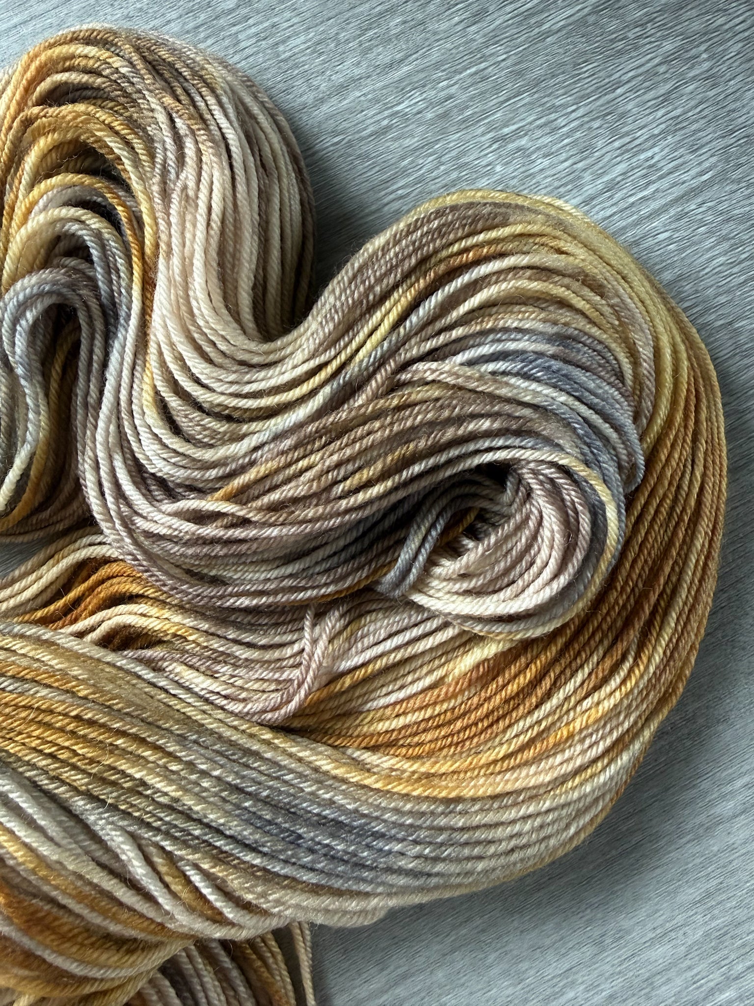 Hand-dyed Mesa ethically sourced merino wool yarn in variegated beige, charcoal, taupe, and toasted ocher.