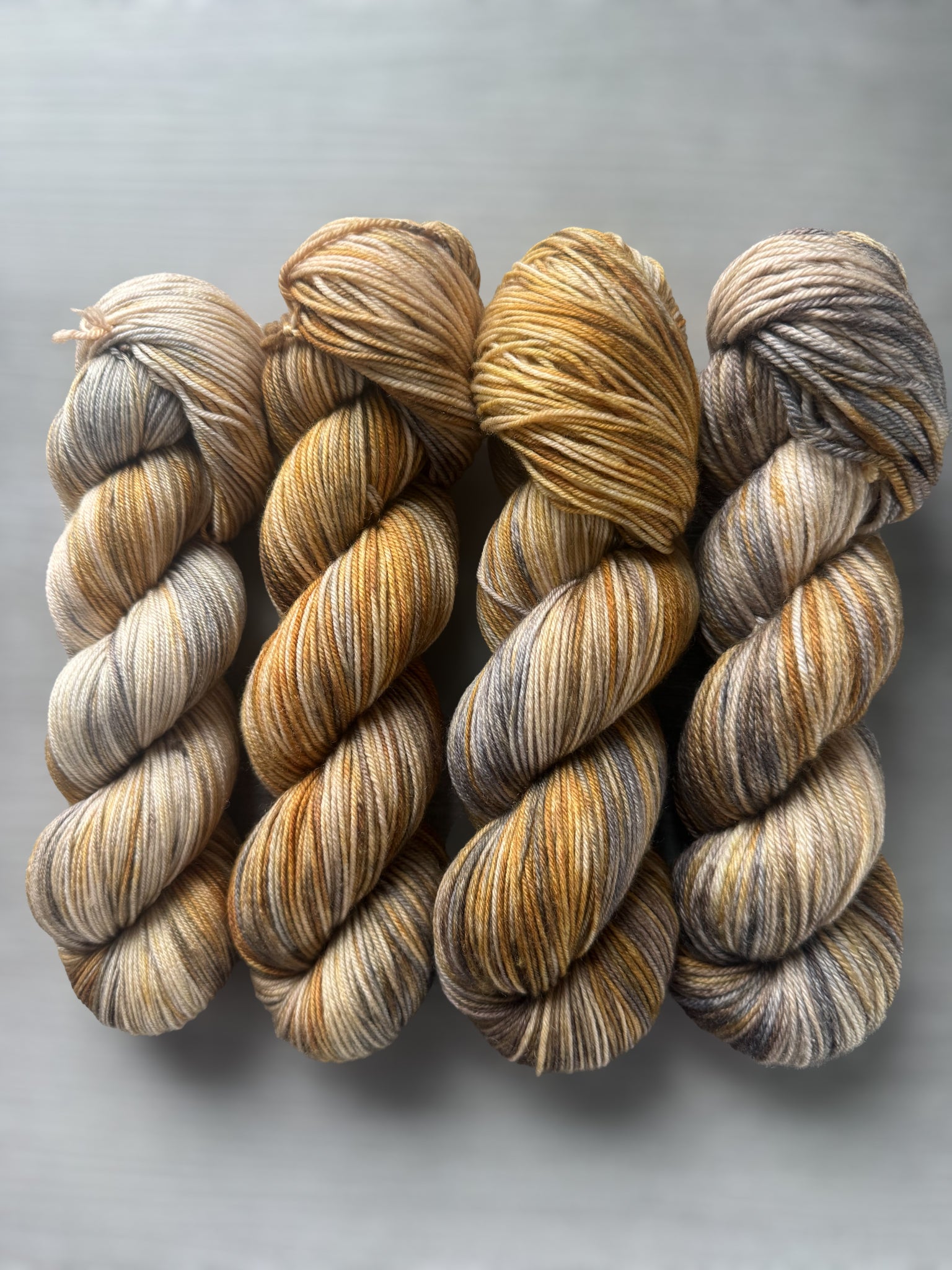 Four skeins of Mesa hand-dyed ethically sourced merino wool yarn with beige, charcoal, taupe, and toasted ocher.