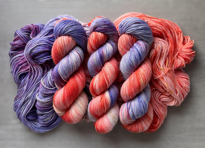 Three skeins of variegated pink and purple yarn on a gray background