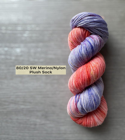Multicolored skein of purple and pink yarn on a gray background with text indicating yarn composition.