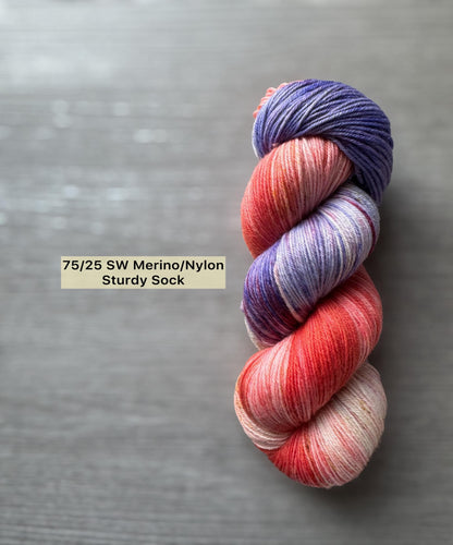 Variegated pink and purple skein of yarn on a gray background with text indicating yarn type.