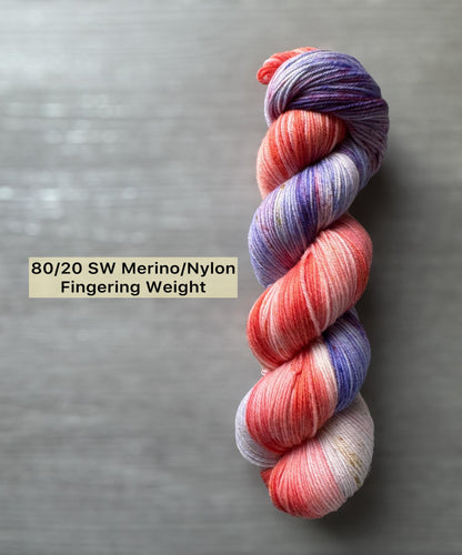 Variegated pink and purple skein of yarn on a gray background with text indicating weight and composition.