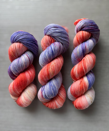 3 skeins of variegated pink and purple yarn on a grey background