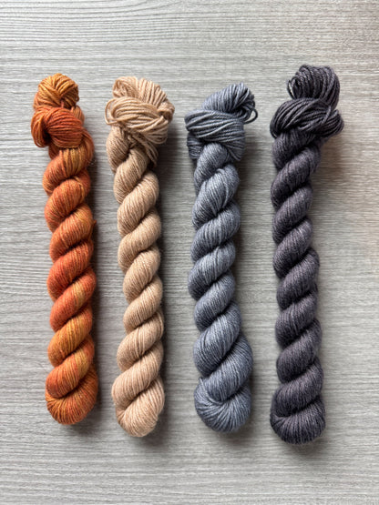 Four skeins of yarn in orange, beige, gray, and black on a textured surface