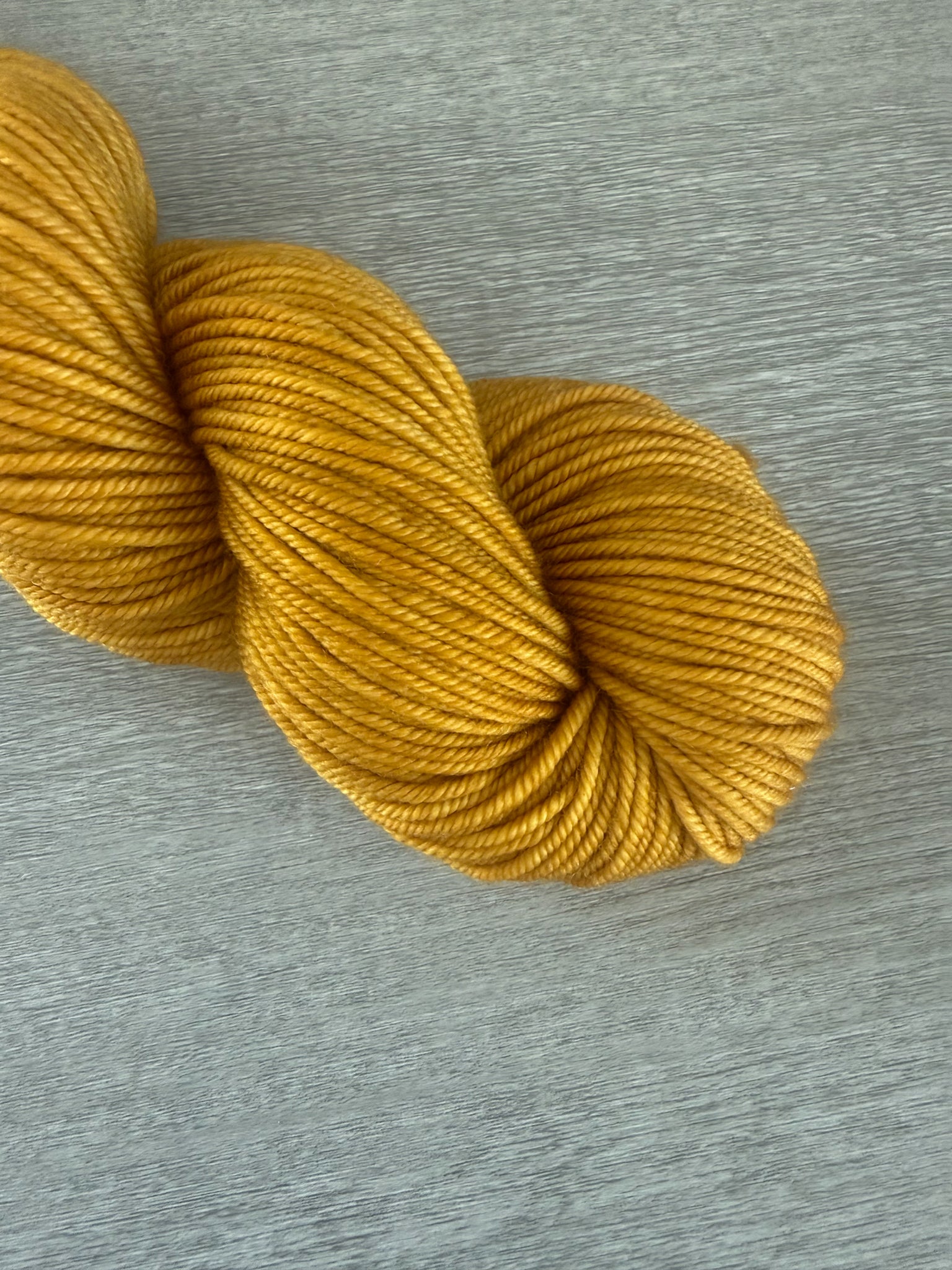 None Of Your Beeswax" hand-dyed golden yellow merino wool yarn skein on a gray surface.