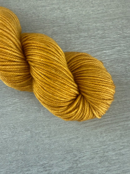 None Of Your Beeswax" hand-dyed golden yellow merino wool yarn skein on a gray surface.