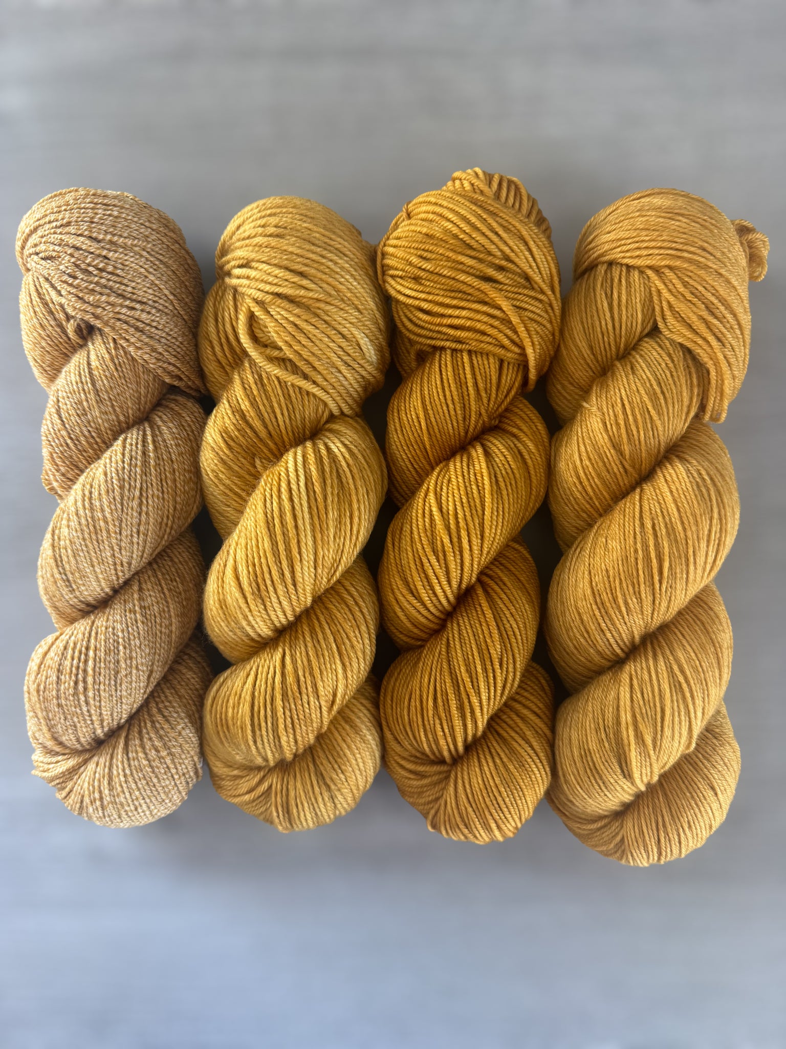 Four skeins of "None Of Your Beeswax" hand-dyed, ethically sourced golden yellow merino wool yarn.