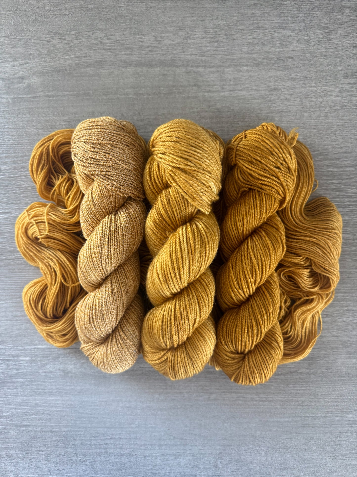 Three skeins of "None Of Your Beeswax" hand-dyed golden yellow merino wool yarn.