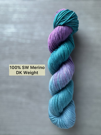 Skein of blue and purple yarn on a gray background with text indicating yarn weight.