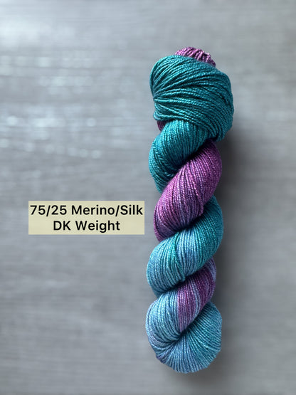 Bicolor blue and purple yarn skein on a gray background with weight and fiber type label.