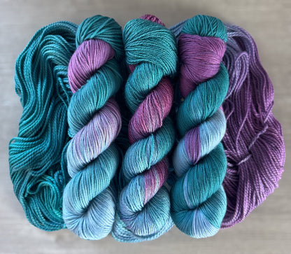 three skeins of yarn with a gradient from teal to purple on a neutral background