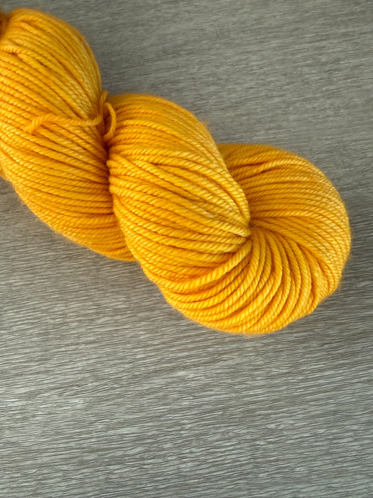 Soleil bright golden yellow hand-dyed ethically sourced merino wool yarn skein on a gray surface.