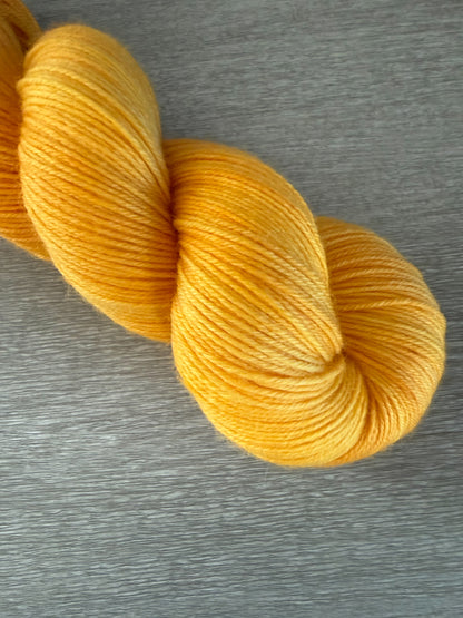 Bright golden yellow Soleil hand-dyed ethically sourced merino wool yarn skein on a gray surface.