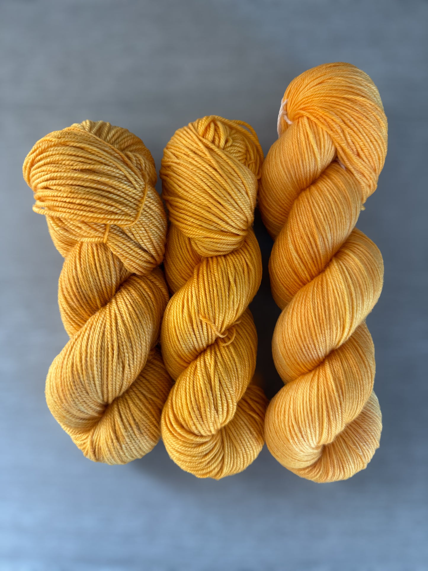 Three skeins of bright golden yellow Soleil hand-dyed ethically sourced merino wool yarn.
