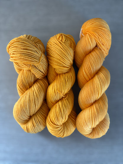 Three skeins of bright golden yellow Soleil hand-dyed ethically sourced merino wool yarn.