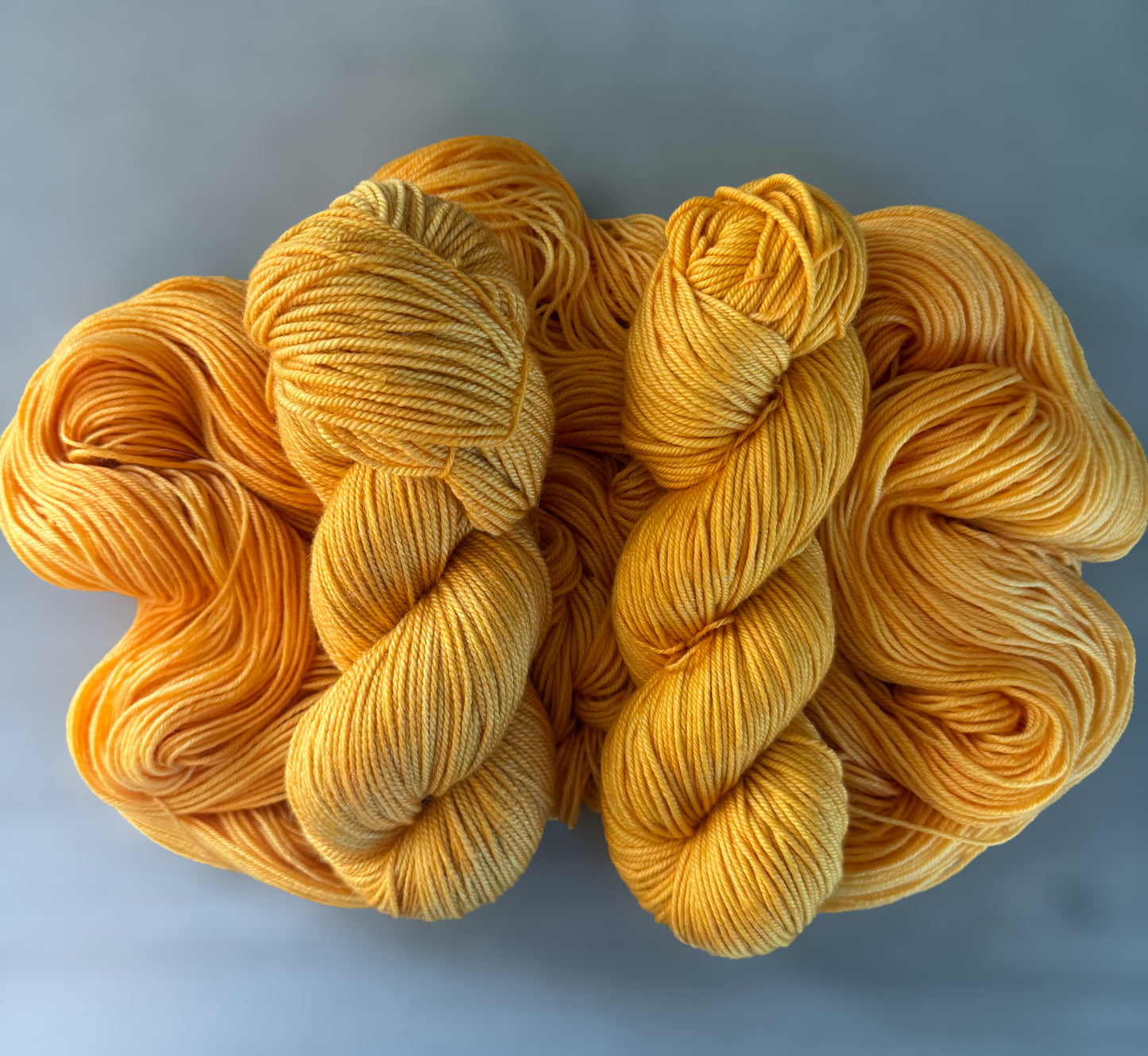 Two skeins of Soleil bright golden yellow hand-dyed ethically sourced merino wool yarn.