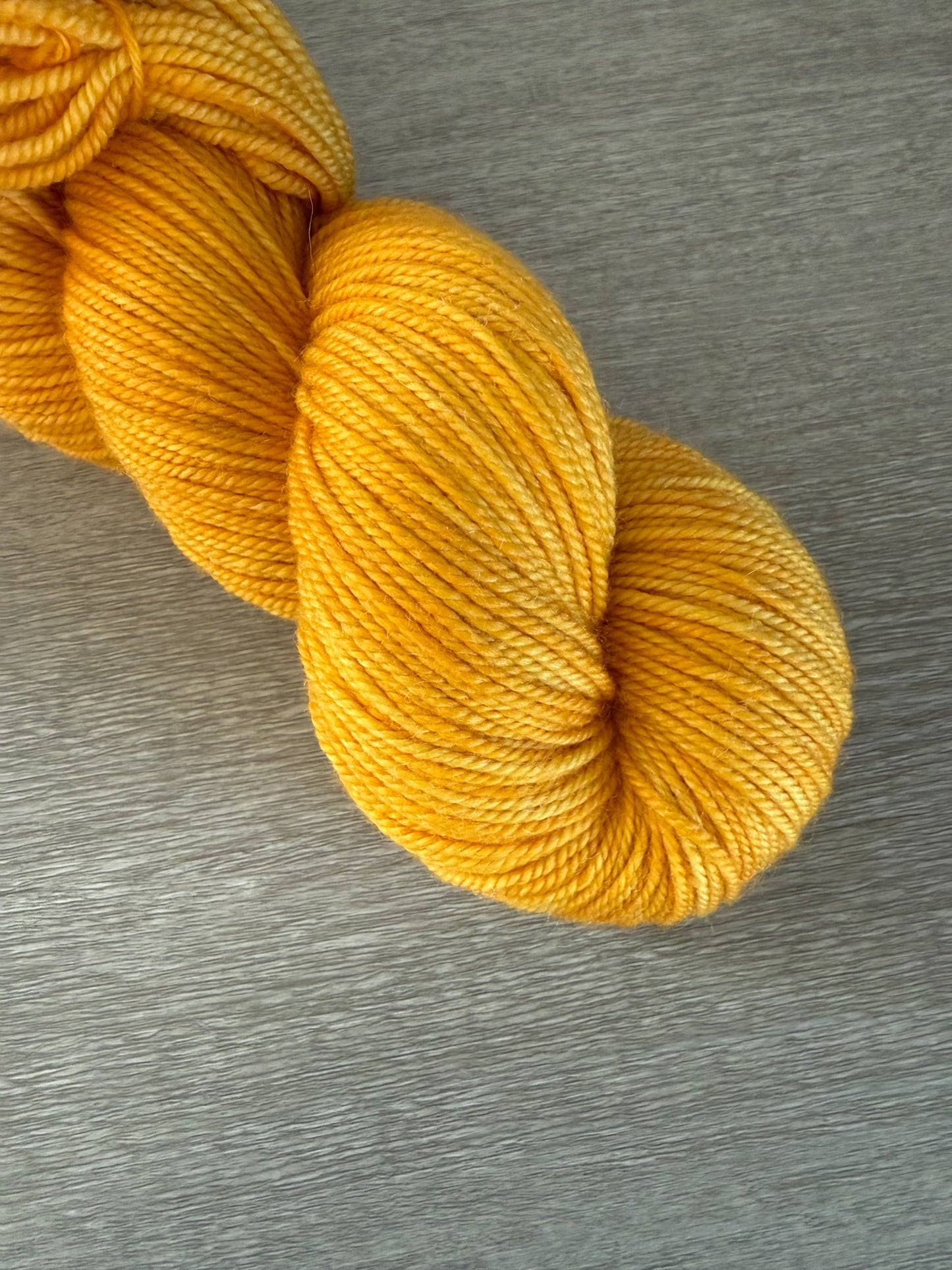 Soleil bright golden yellow hand-dyed ethically sourced merino wool yarn skein on a gray surface.