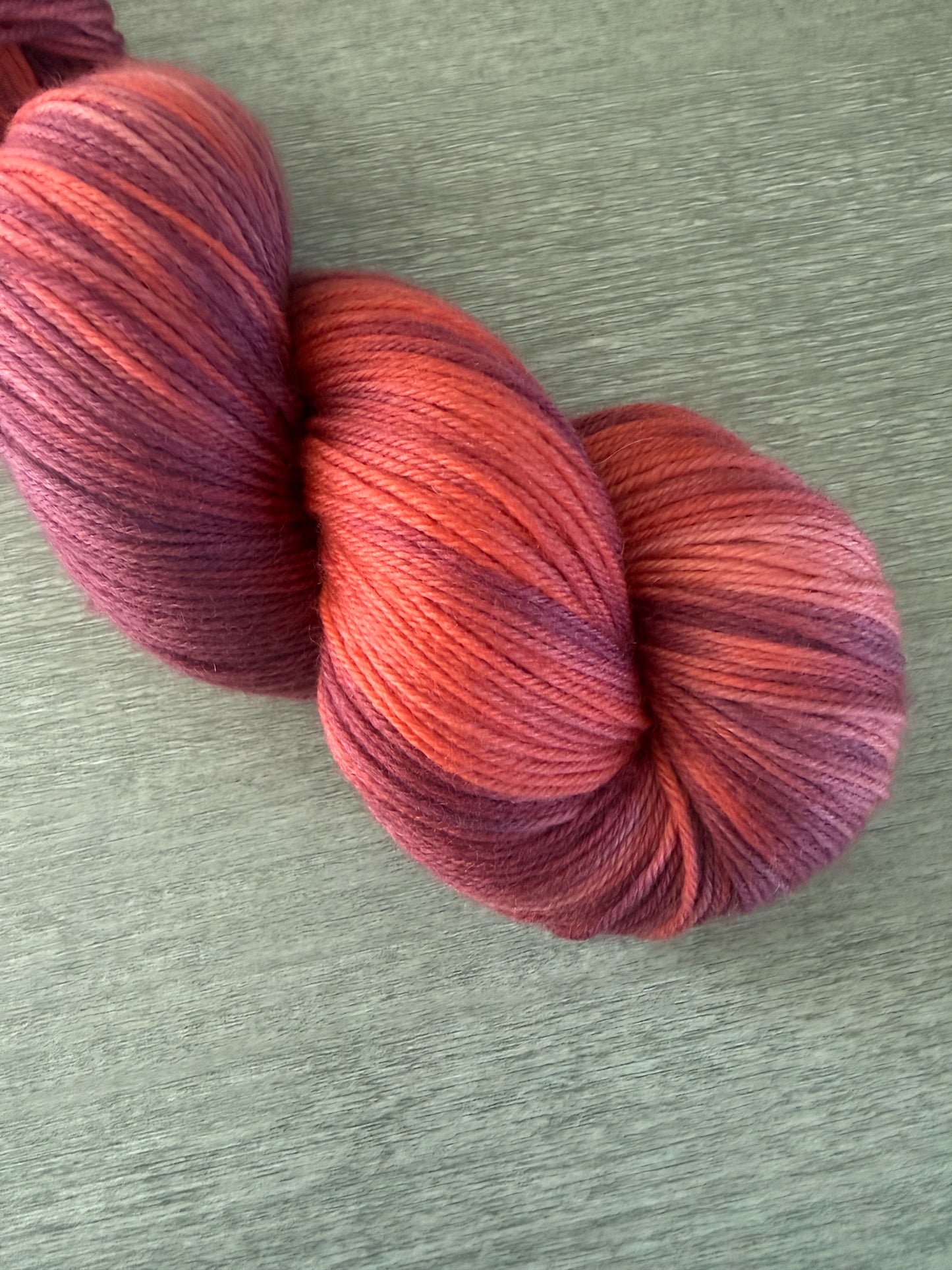 Ethically sourced merino wool yarn in "Summer Fling" with variegated burgundy, red, and orange hues.