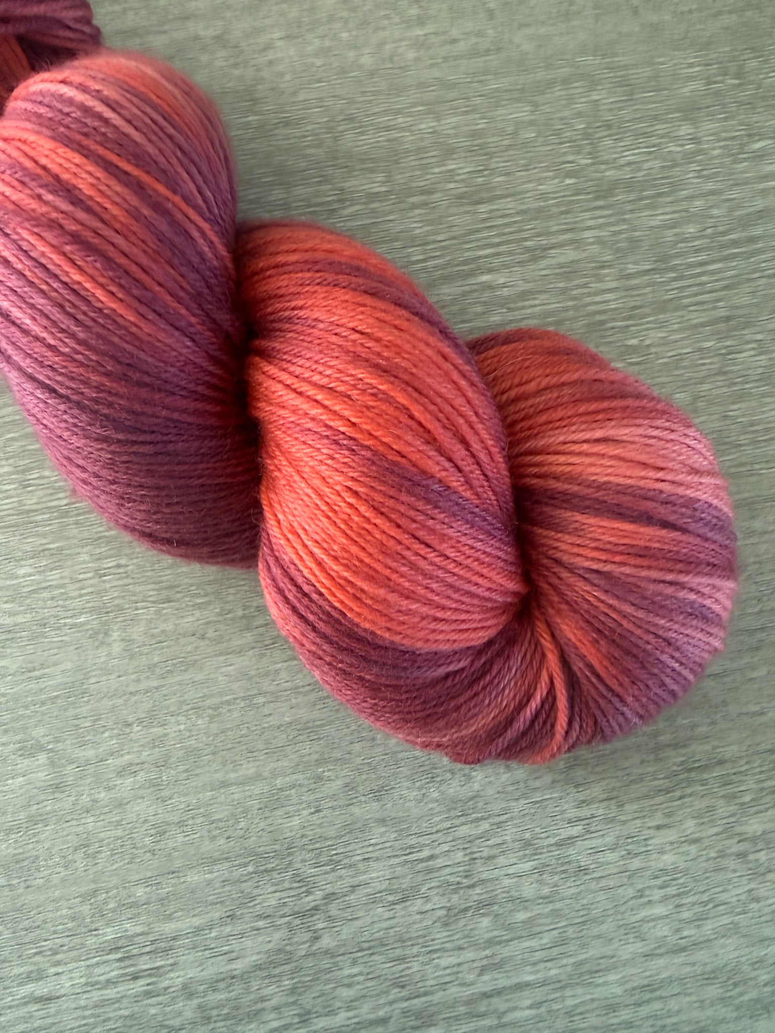 Ethically sourced merino wool yarn in "Summer Fling" with variegated burgundy, red, and orange hues.