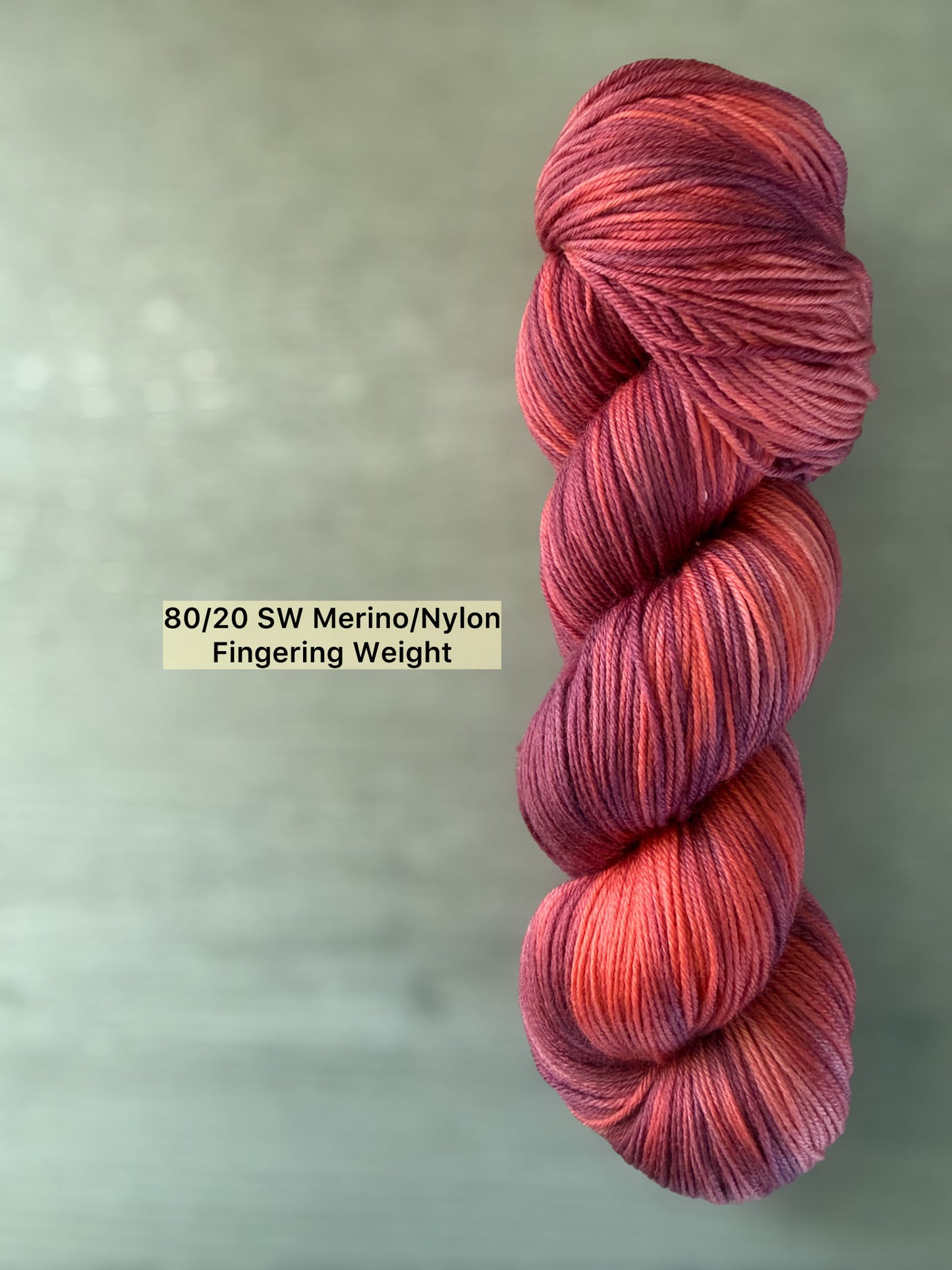 Skein of ethically sourced Summer Fling variegated merino wool yarn in burgundy, red, and orange sunset hues.