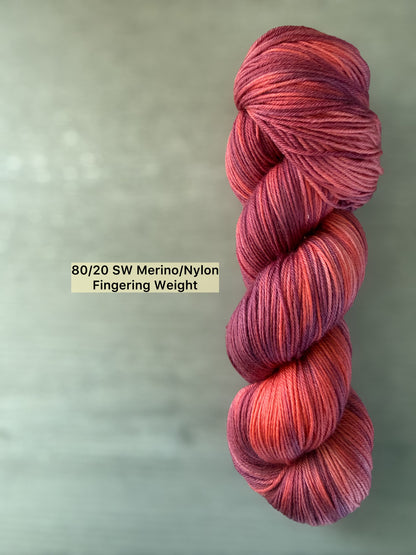 Skein of ethically sourced Summer Fling variegated merino wool yarn in burgundy, red, and orange sunset hues.