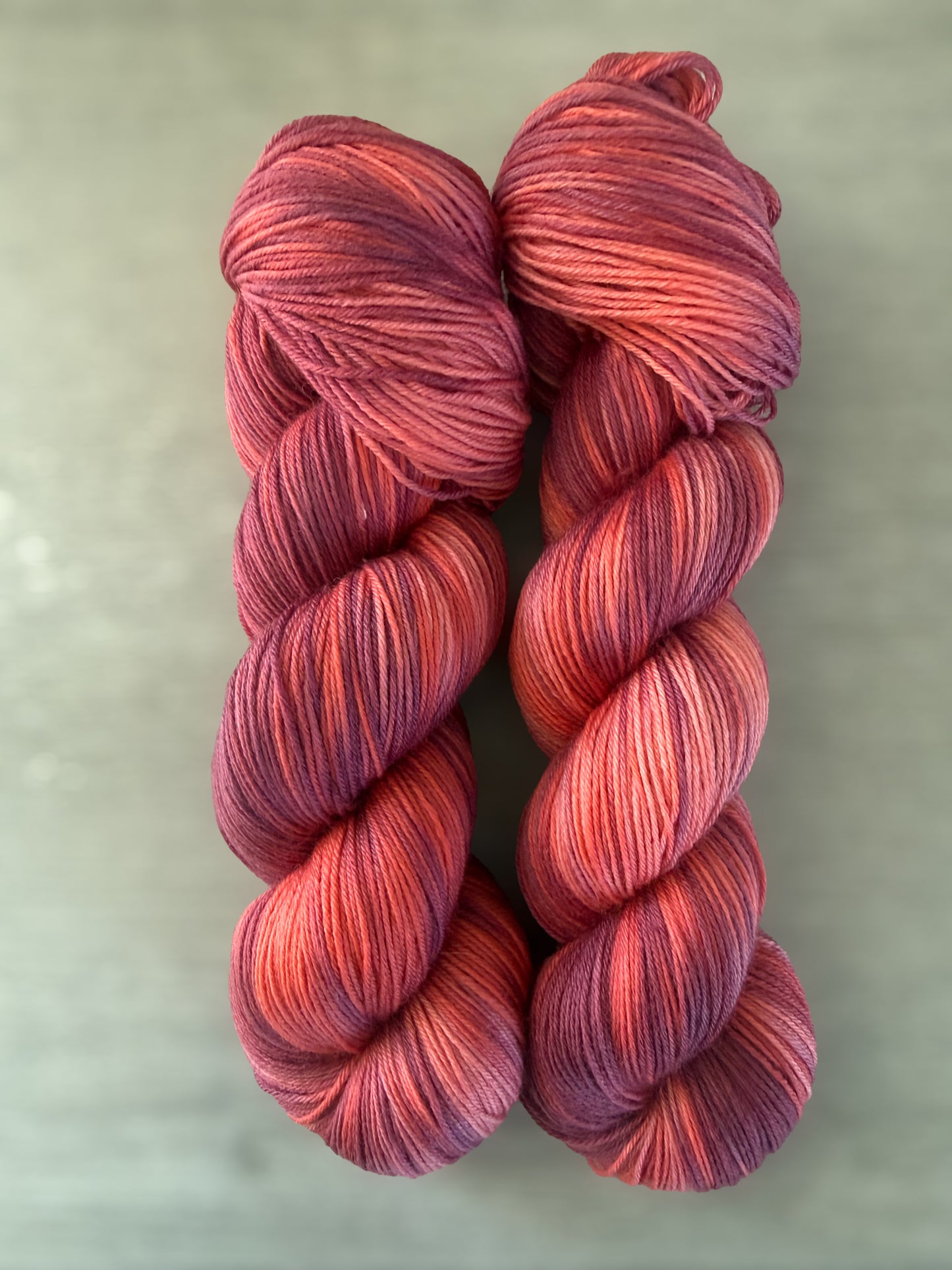 Two skeins of ethically sourced "Summer Fling" hand-dyed merino wool yarn in variegated burgundy, red, and orange.