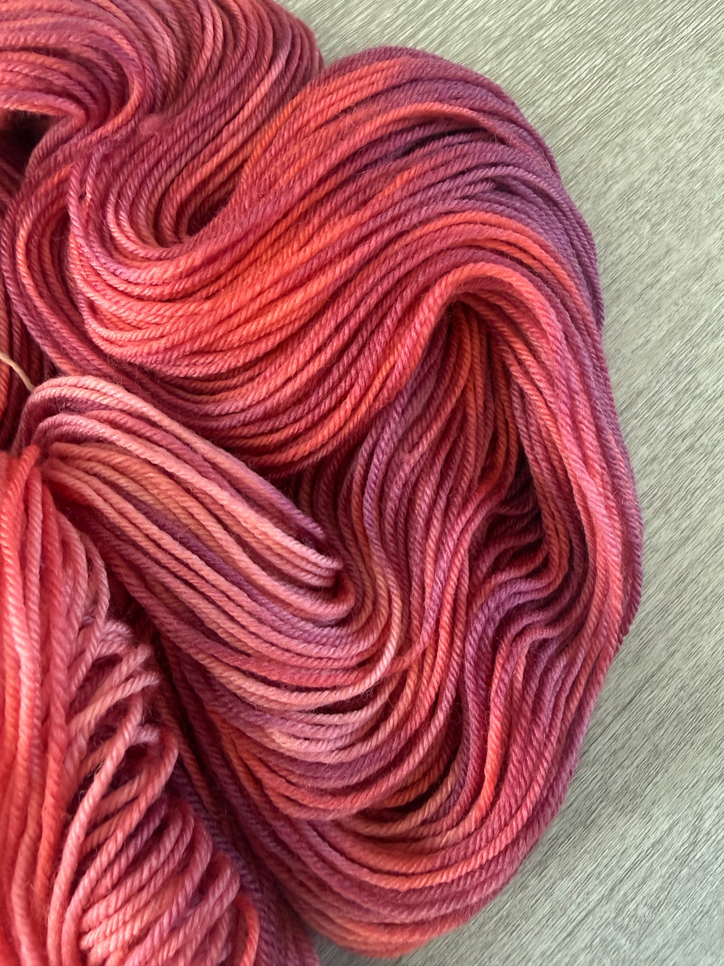 Ethically sourced merino wool yarn in "Summer Fling" with variegated burgundy, red, and orange hues.
