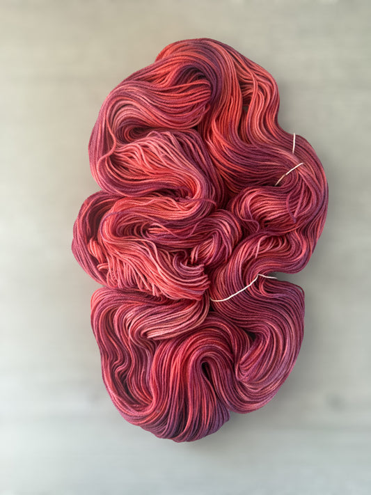 Ethically sourced merino wool yarn in "Summer Fling" with variegated burgundy, red, and orange hues.