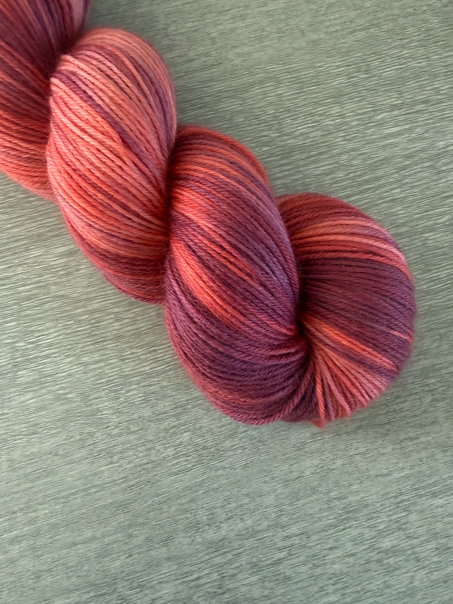 Skein of ethically sourced merino wool yarn in "Summer Fling" with variegated burgundy, red, and orange hues.