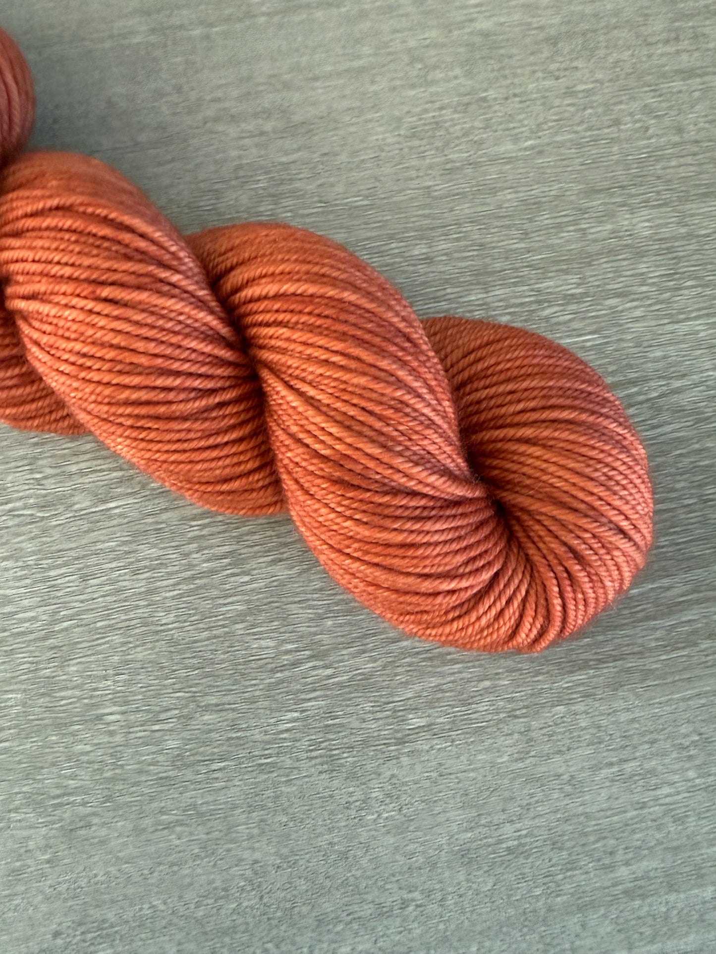 Skein of ethically sourced, hand-dyed terracotta merino wool yarn with warm, reddish-brown semi-solid hues.