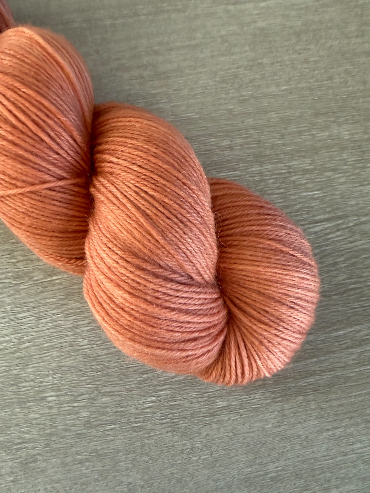 Skein of ethically sourced, hand-dyed terracotta merino wool yarn with warm, reddish-brown hues.