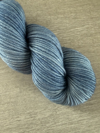 Hand-dyed West Bay blue tonal ethically sourced merino wool yarn skein on a light wood surface.
