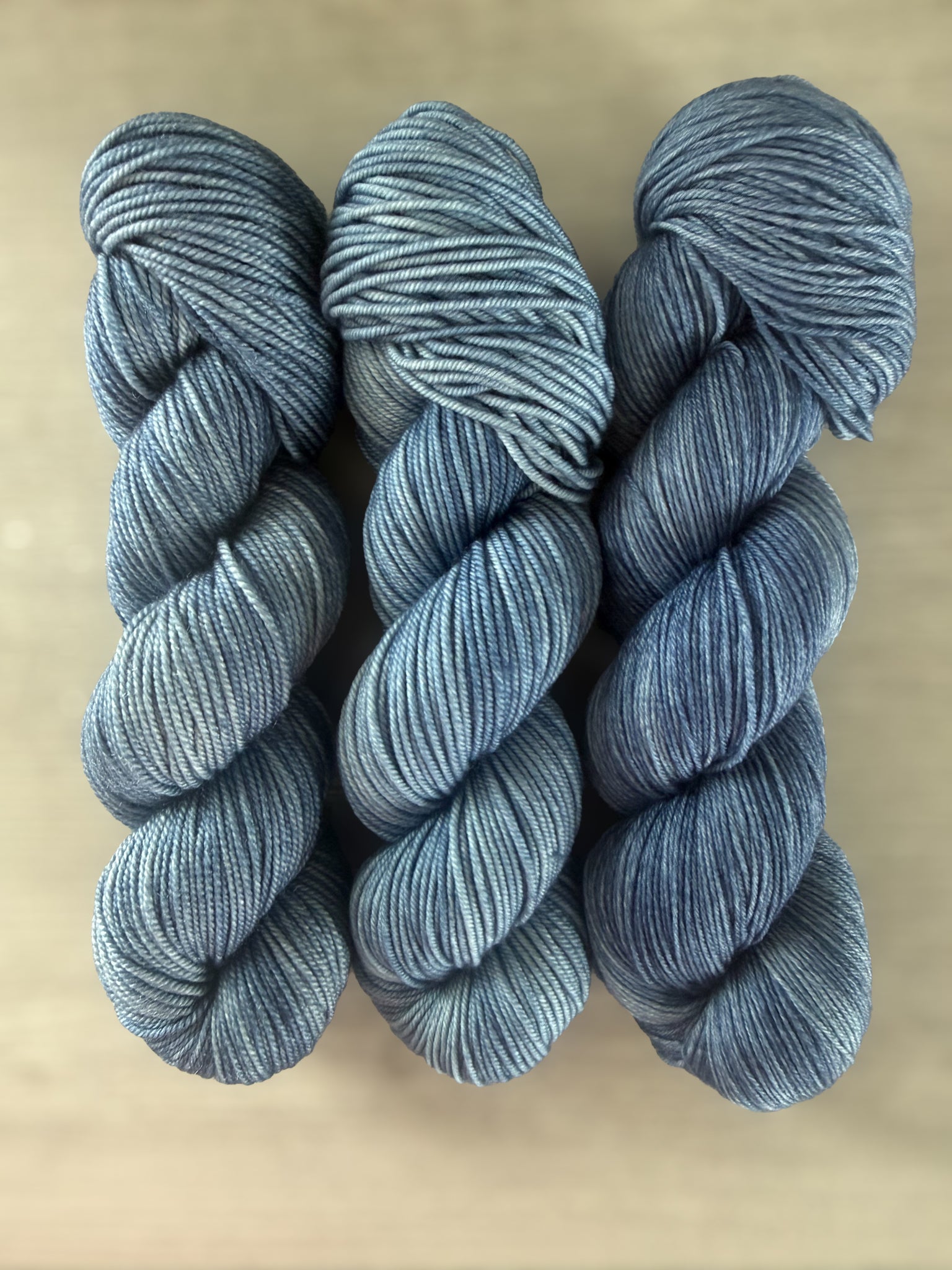 Three skeins of West Bay artisan hand-dyed ethically sourced merino wool yarn in serene blue tonal shades.