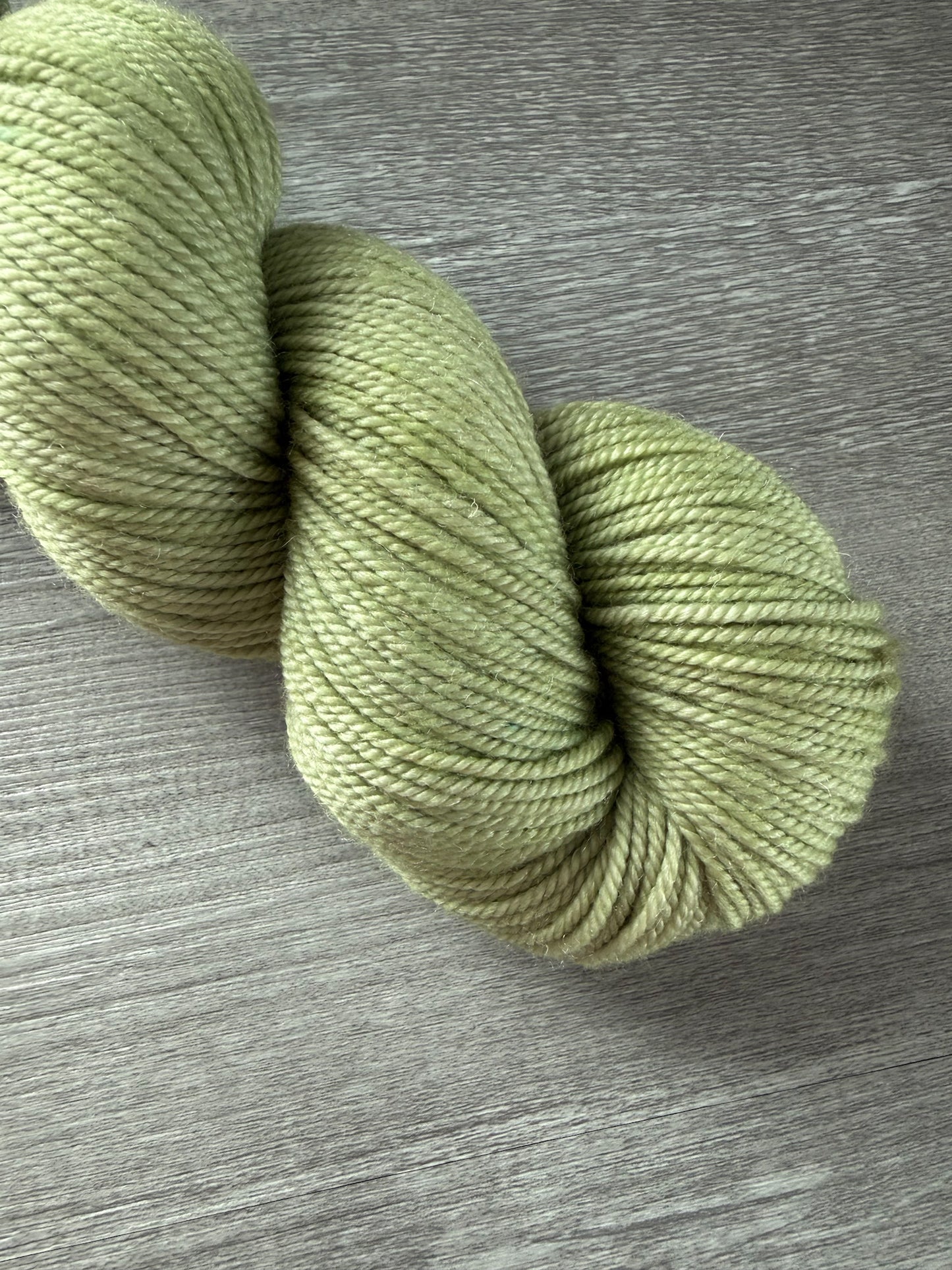 Vibrant lime green, hand-dyed, ethically sourced merino wool yarn skein on a wooden surface.