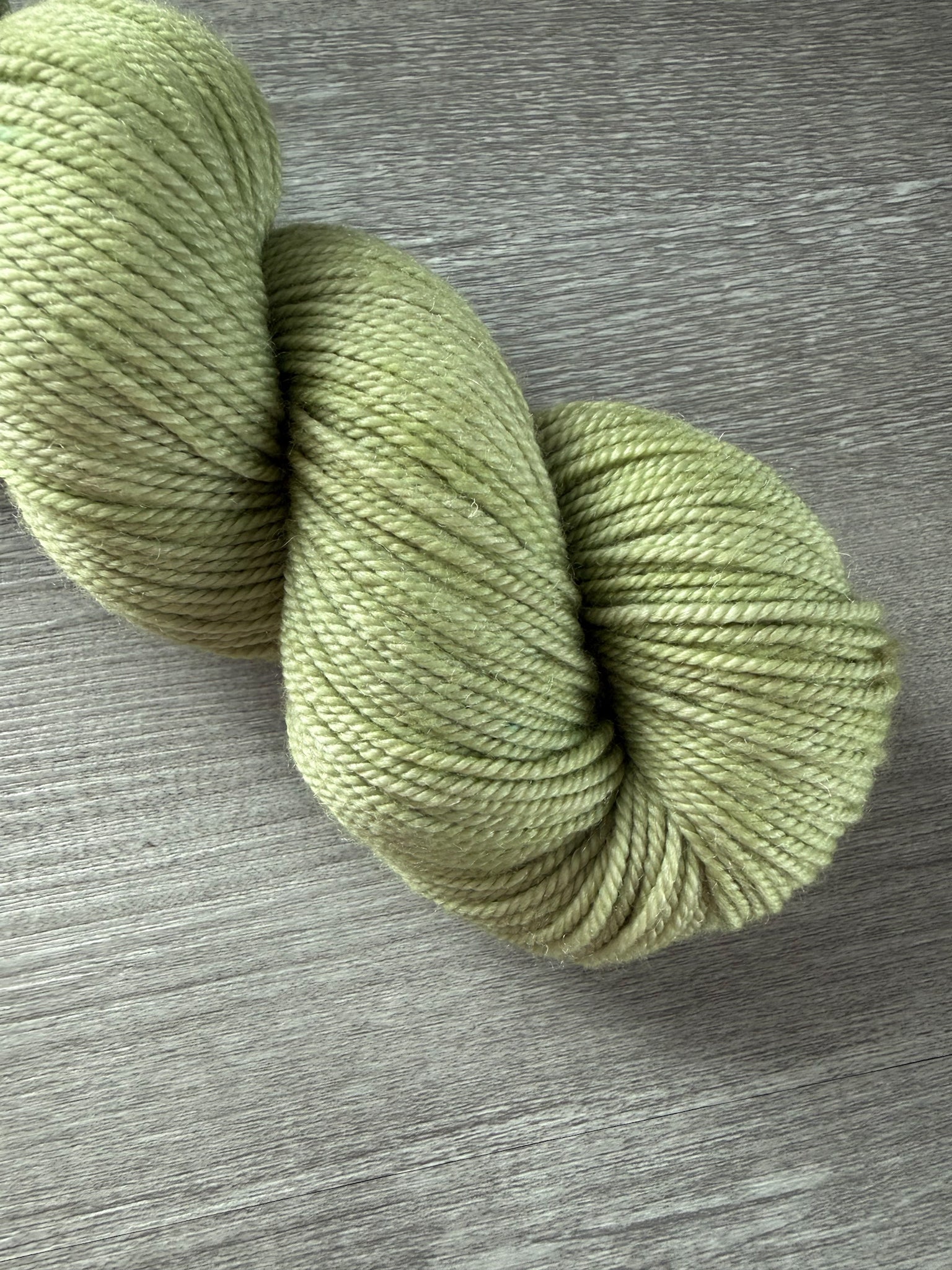 Vibrant lime green, hand-dyed, ethically sourced merino wool yarn skein on a wooden surface.