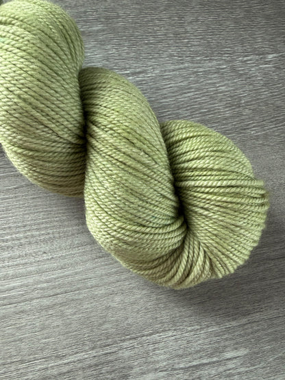 Vibrant lime green, hand-dyed, ethically sourced merino wool yarn skein on a wooden surface.