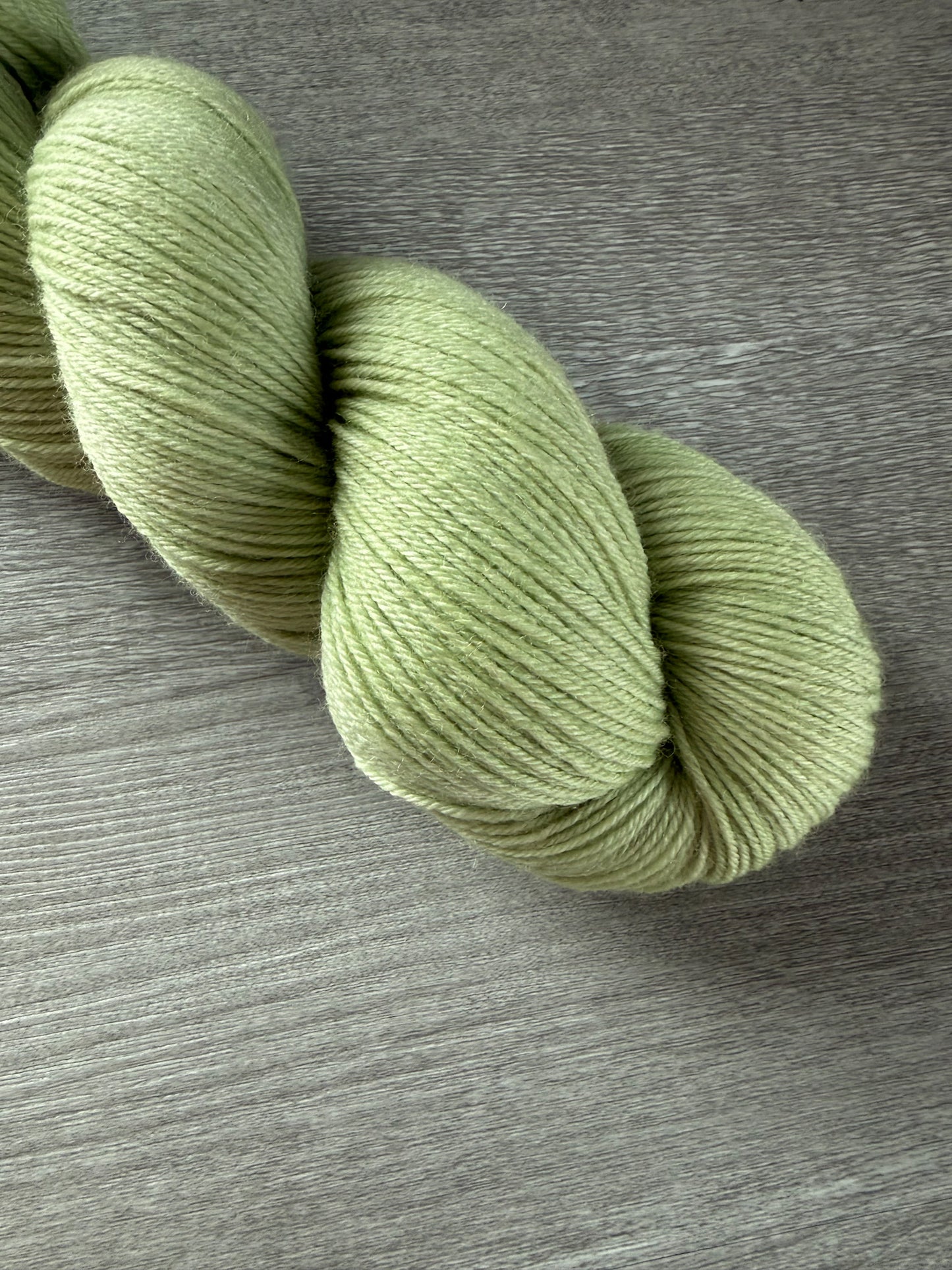 Vibrant lime green hand-dyed ethically sourced merino wool yarn skein on a gray wood surface.