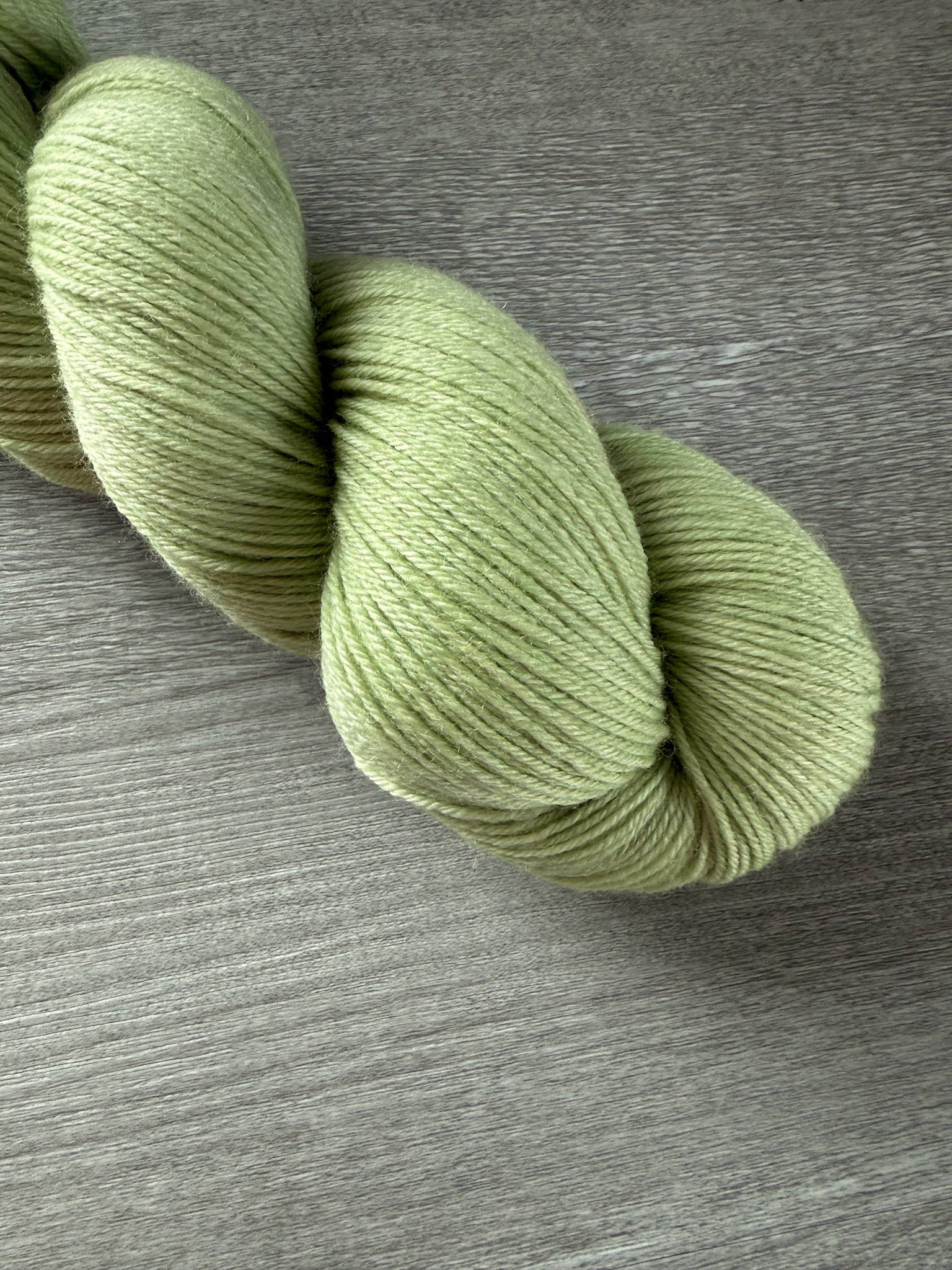 Vibrant lime green hand-dyed ethically sourced merino wool yarn skein on a gray wood surface.