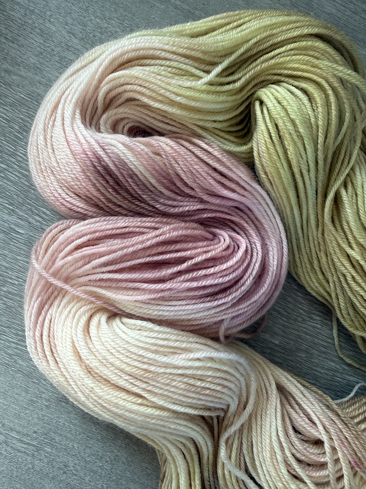 Ethically sourced merino wool yarn in soft dusty pink, warm golden yellow, and light tan watercolor hues.