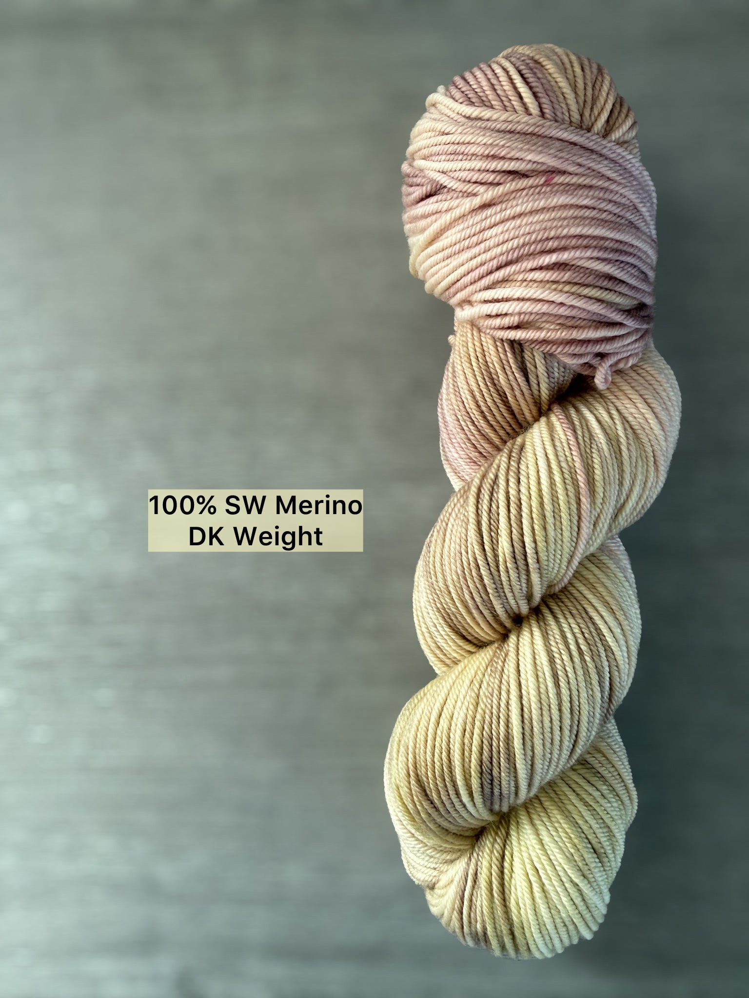 Ethically sourced hand-dyed merino wool yarn in dusty pink, golden yellow, and light tan watercolor blend.