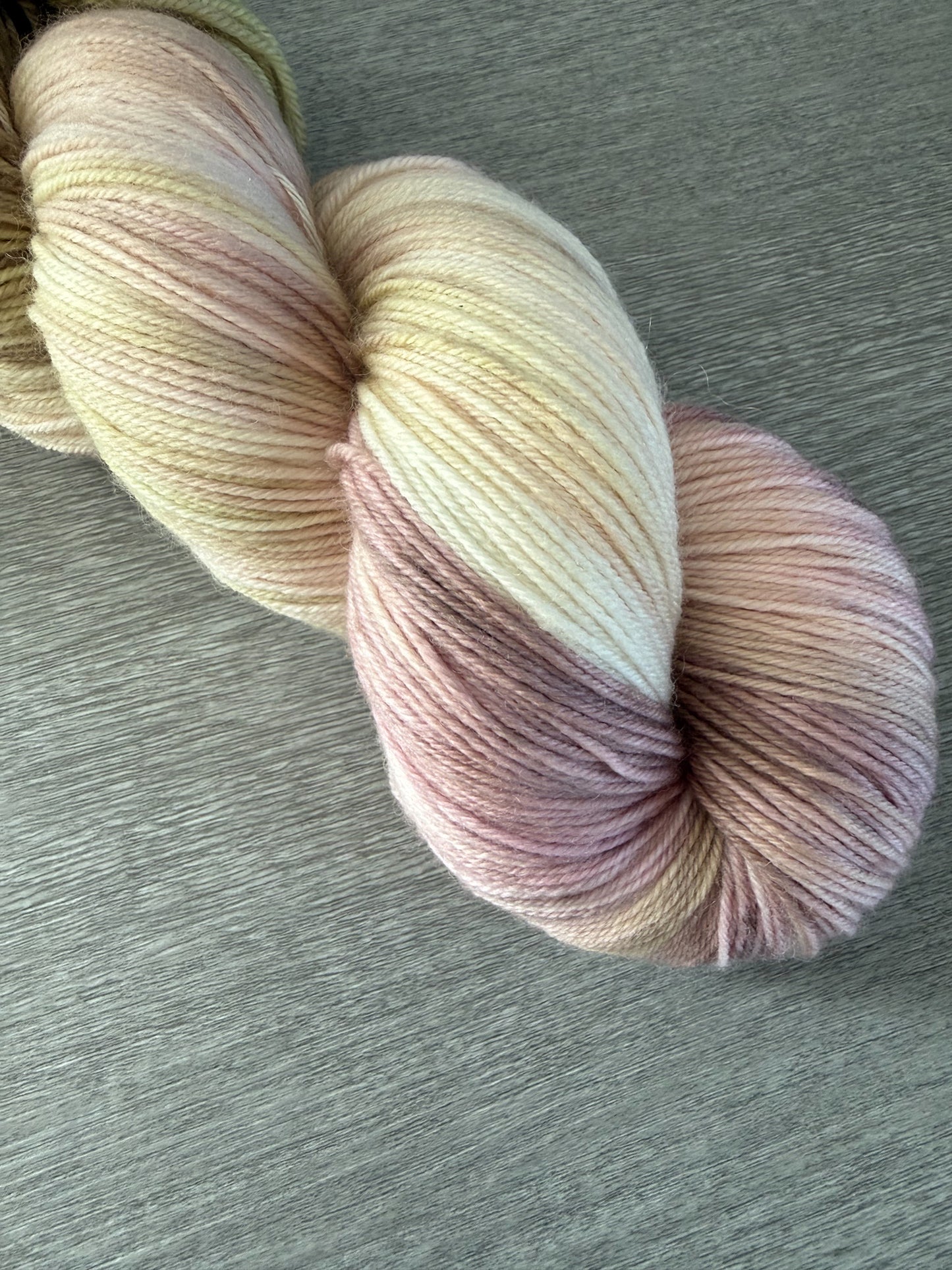 Ethically sourced hand-dyed merino wool yarn in soft dusty pink, golden yellow, and light tan watercolor hues.