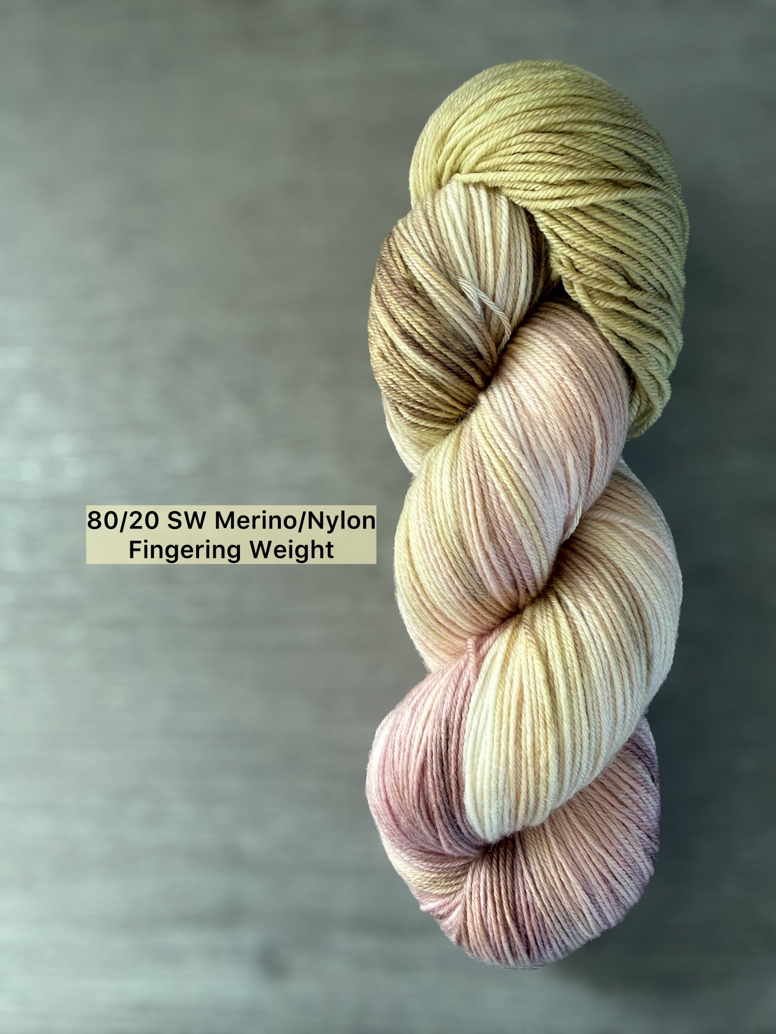 Ethically sourced hand-dyed merino wool yarn in dusty pink, golden yellow, and light tan watercolor blend.