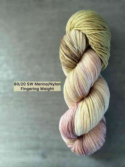 Ethically sourced hand-dyed merino wool yarn in dusty pink, golden yellow, and light tan watercolor blend.