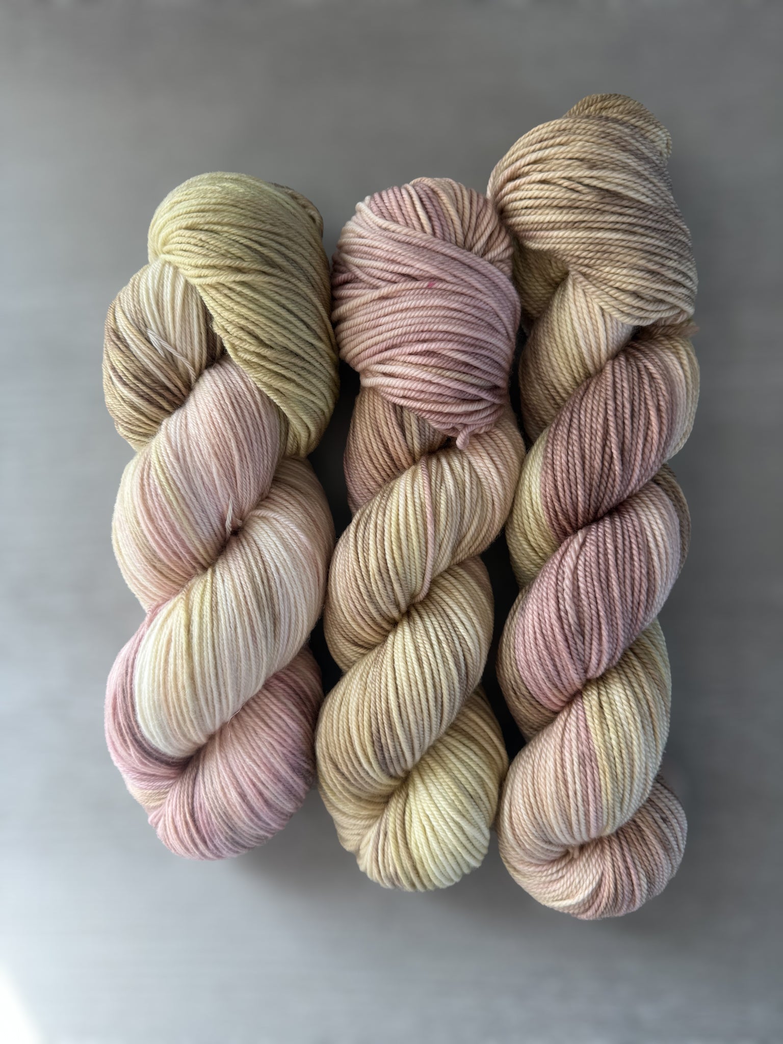 Three skeins of ethically sourced merino wool yarn, hand-dyed in dusty pink, golden yellow, and light tan.