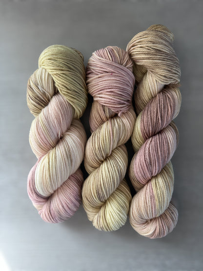 Three skeins of ethically sourced merino wool yarn, hand-dyed in dusty pink, golden yellow, and light tan.
