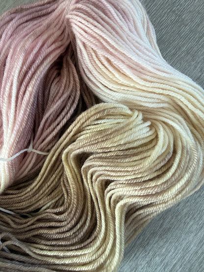 Ethically sourced merino wool yarn, hand-dyed in dusty pink, golden yellow, and light tan watercolor hues.