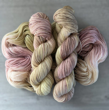 Ethically sourced merino wool yarn, hand-dyed in dusty pink, golden yellow, and light tan watercolor hues.