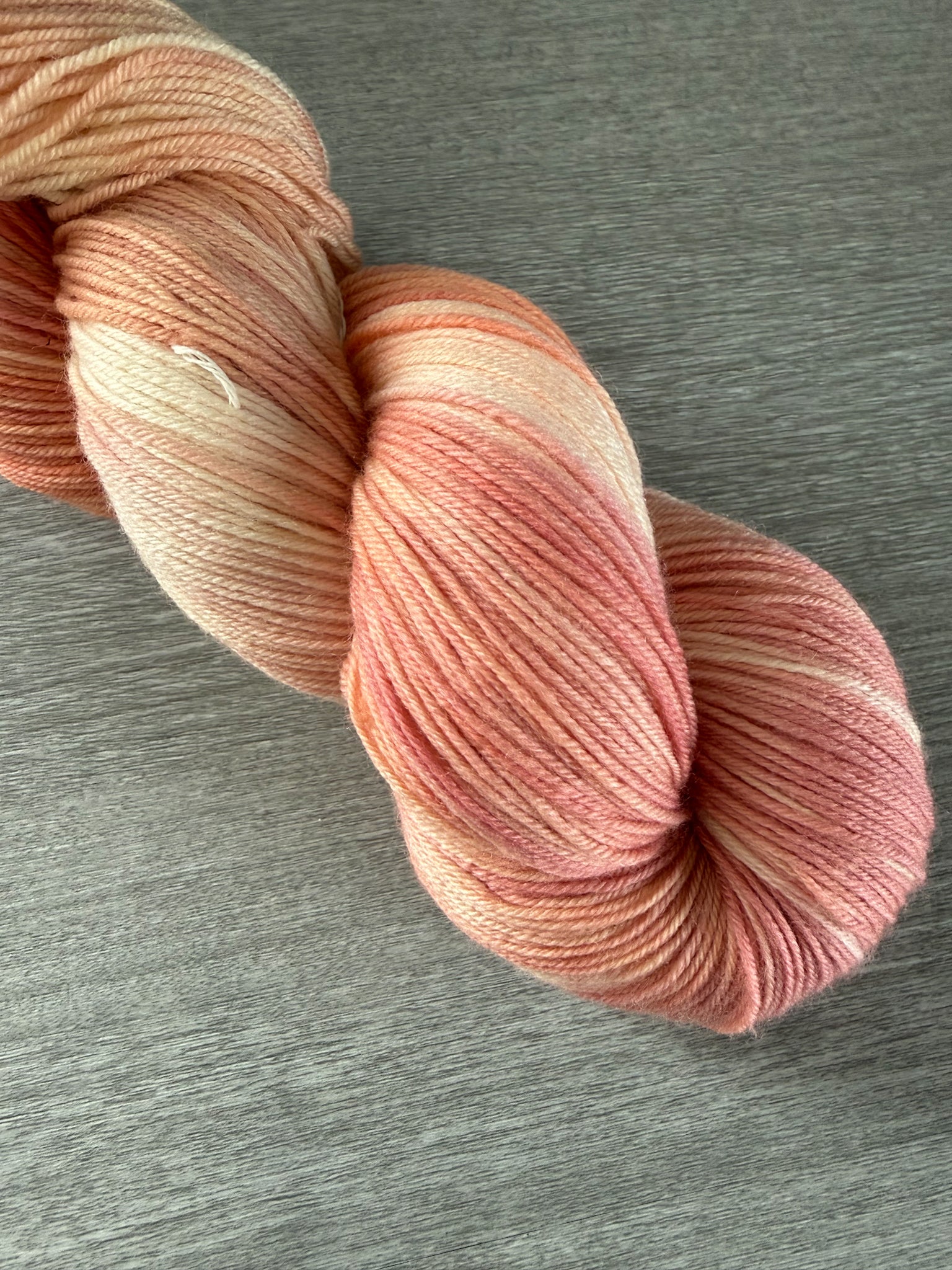 Hand-dyed Whispering Petals ethically sourced merino wool yarn in soft peach, ivory, and rose hues.