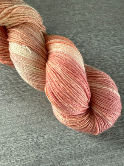 Hand-dyed Whispering Petals ethically sourced merino wool yarn in soft peach, ivory, and rose hues.