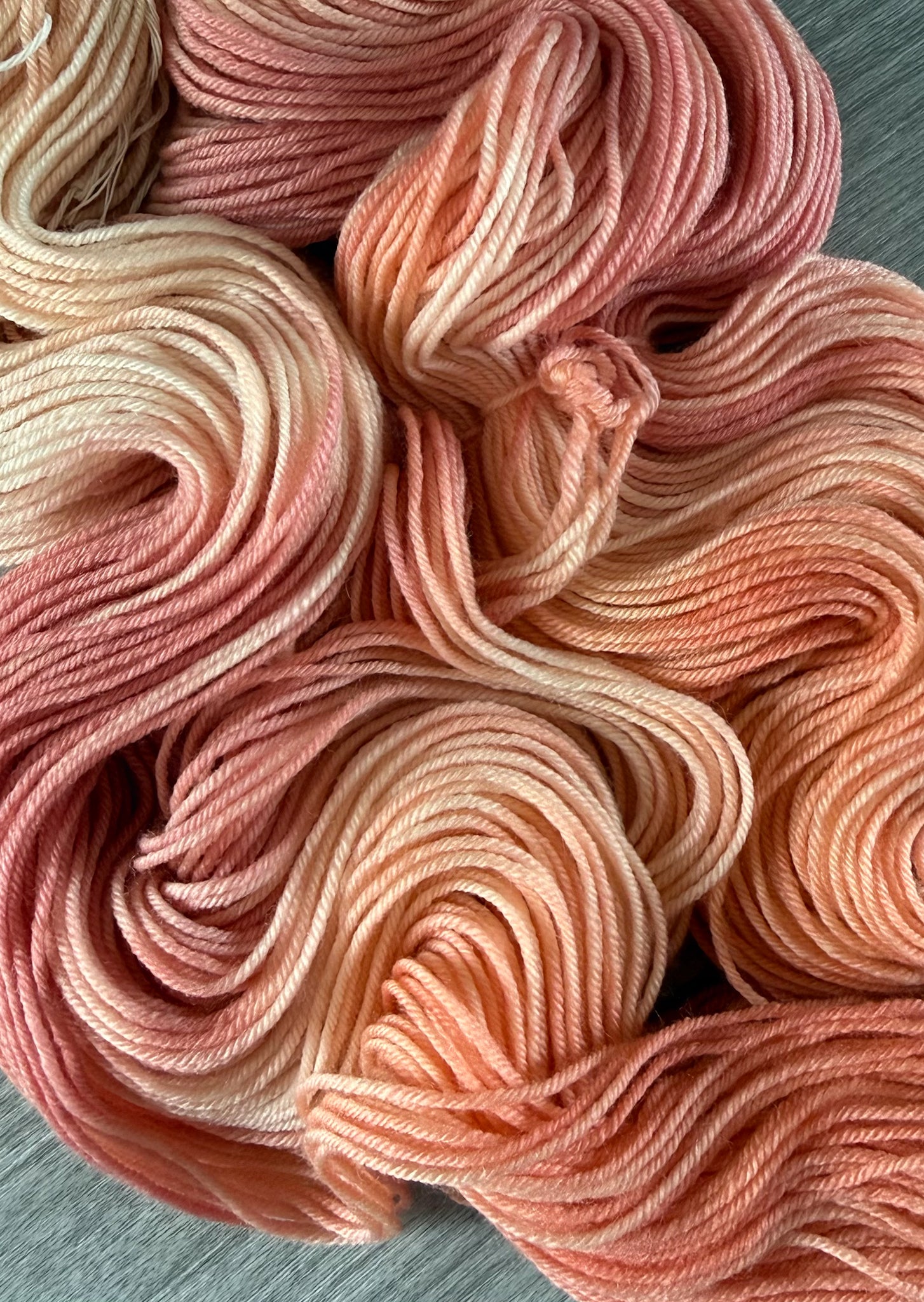 Ethically sourced merino wool yarn, hand-dyed in soft peach, ivory, and light rose watercolor hues.